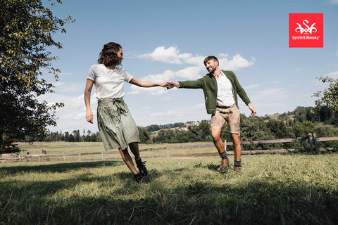 Trachtenstrickjacke kombiniert mit wei&szlig;em Trachtenhemd und Lederhose, Sie tr&auml;gt einen Sommerlichen Trachtenrock und eine wei&szlig;e Bluse